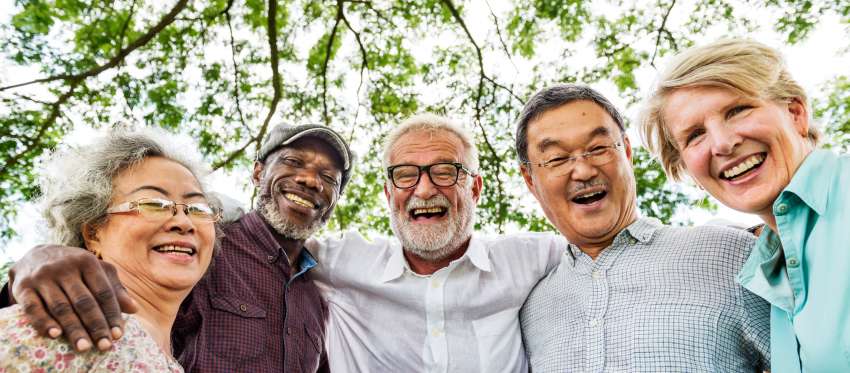 A smiling group of retirement-age people stand with their arms around one another's shoulders.
